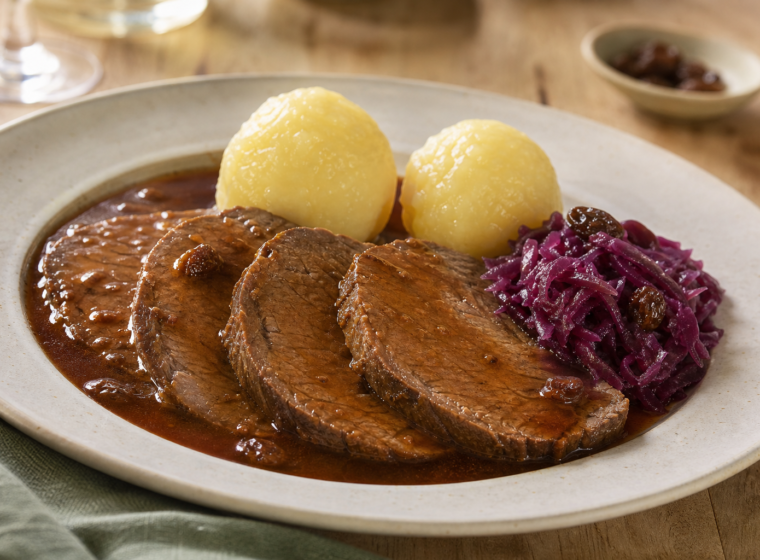 Fatias de Sauerbraten com molho escuro, bolinhos de batata e repolho roxo